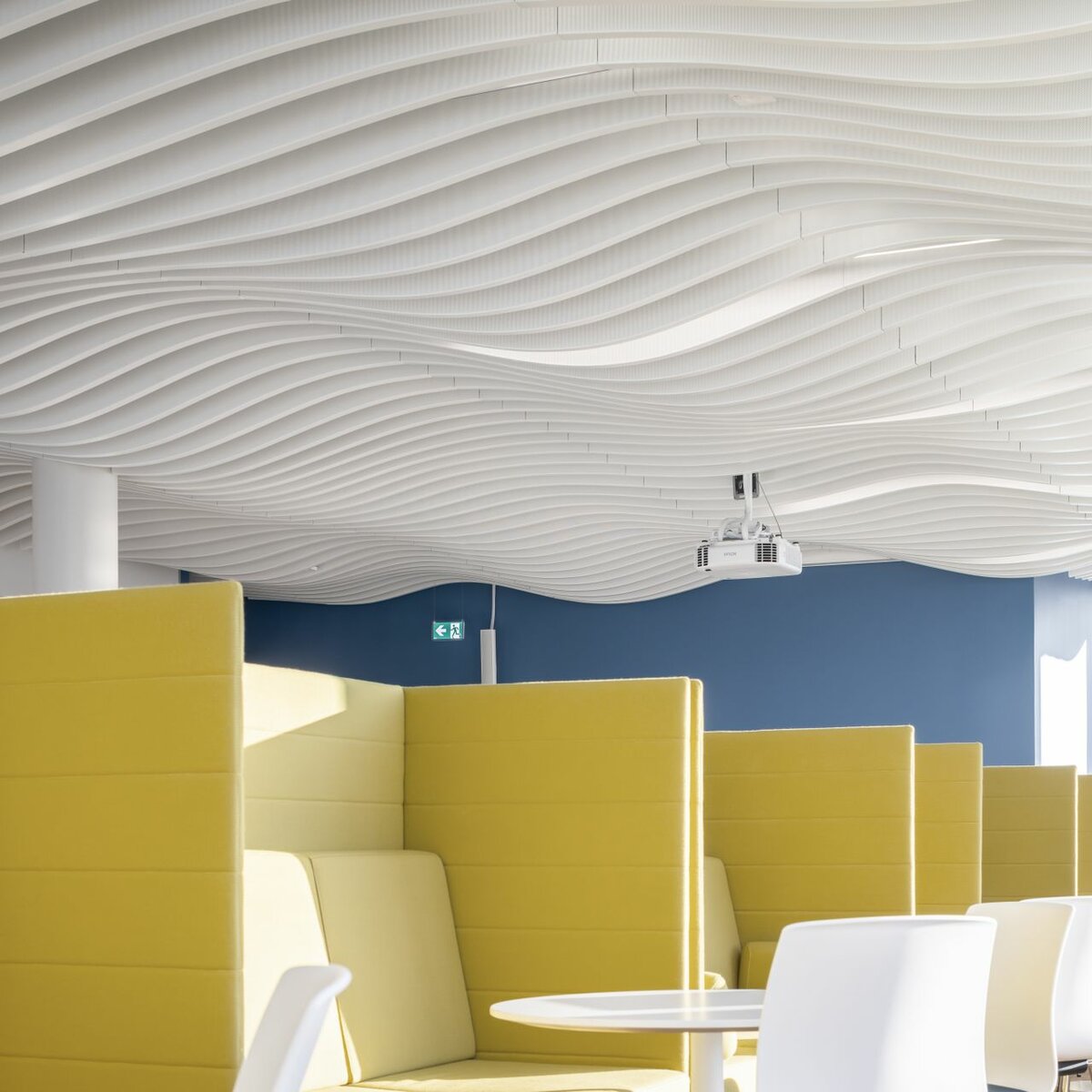 Moderne Kantine im Bürogebäude mit markanter Lamellendecke von Lindner und gelben Sitznischen für eine inspirierende Pausenatmosphäre.