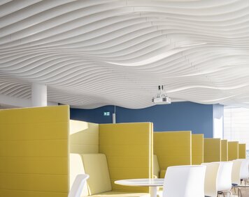 Moderne Kantine im Bürogebäude mit markanter Lamellendecke von Lindner und gelben Sitznischen für eine inspirierende Pausenatmosphäre.