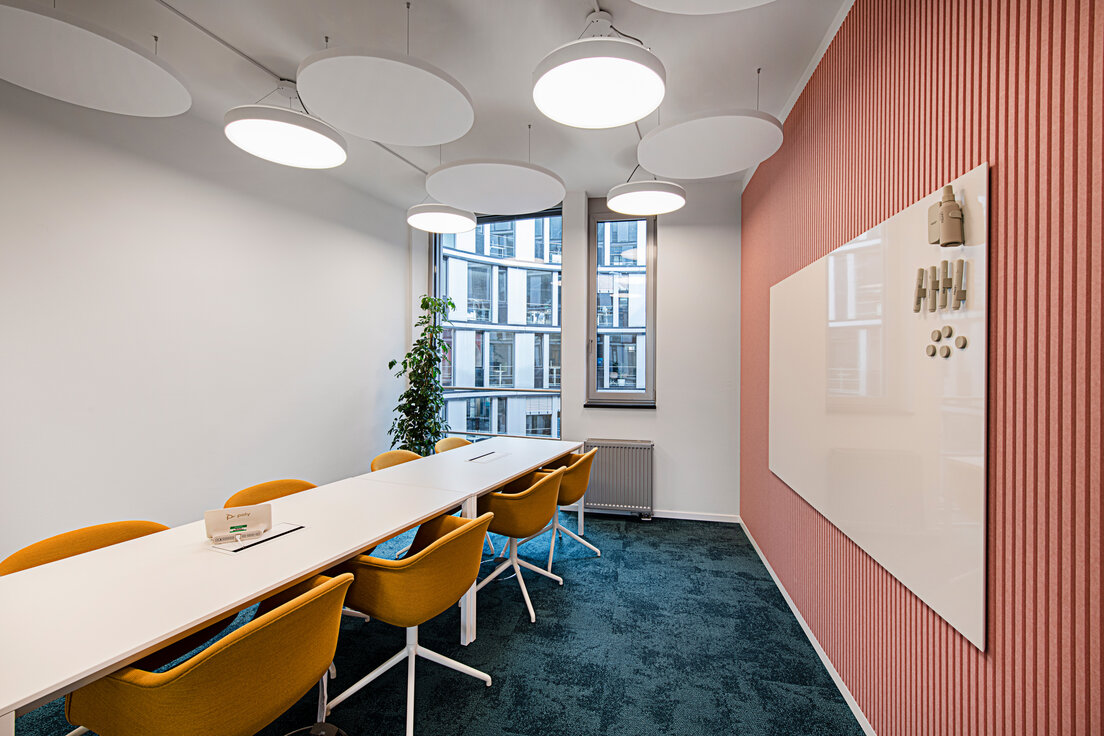 Colorful modern meeting room with white tables, sun-yellow upholstered chairs, navy velvet carpet, pink rose wood slat wall with whiteboard, round pendant lights, and long windows in background