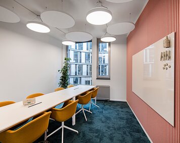  In einem Besprechungsraum steht ein großer Tisch, umringt von einer Vielzahl von Stühlen, während an der Wand eine Magnetwand angebracht ist.