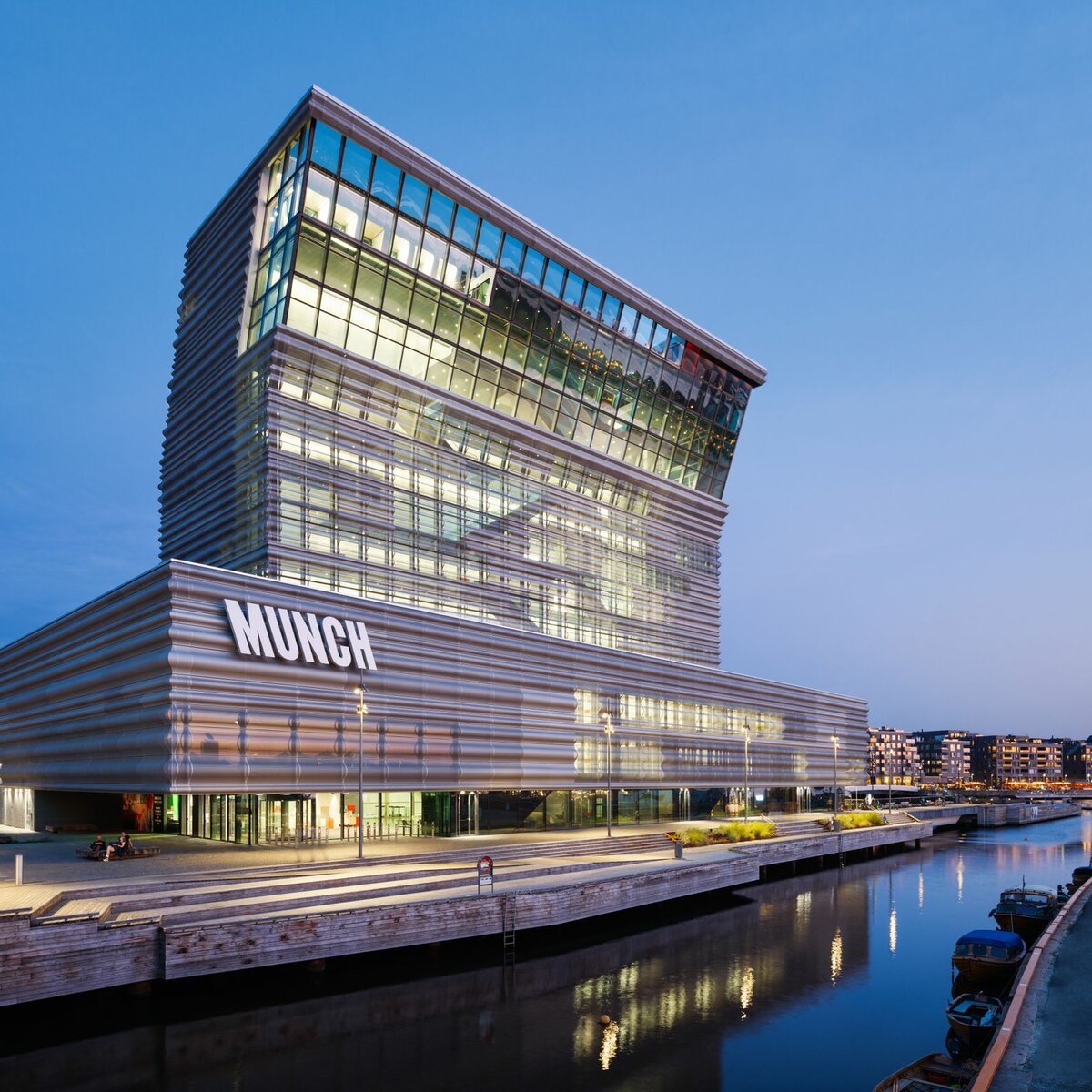 MUNCH Museum Oslo mit wellenförmiger Aluminiumfassade und Glasfront bei Abenddämmerung am Wasser