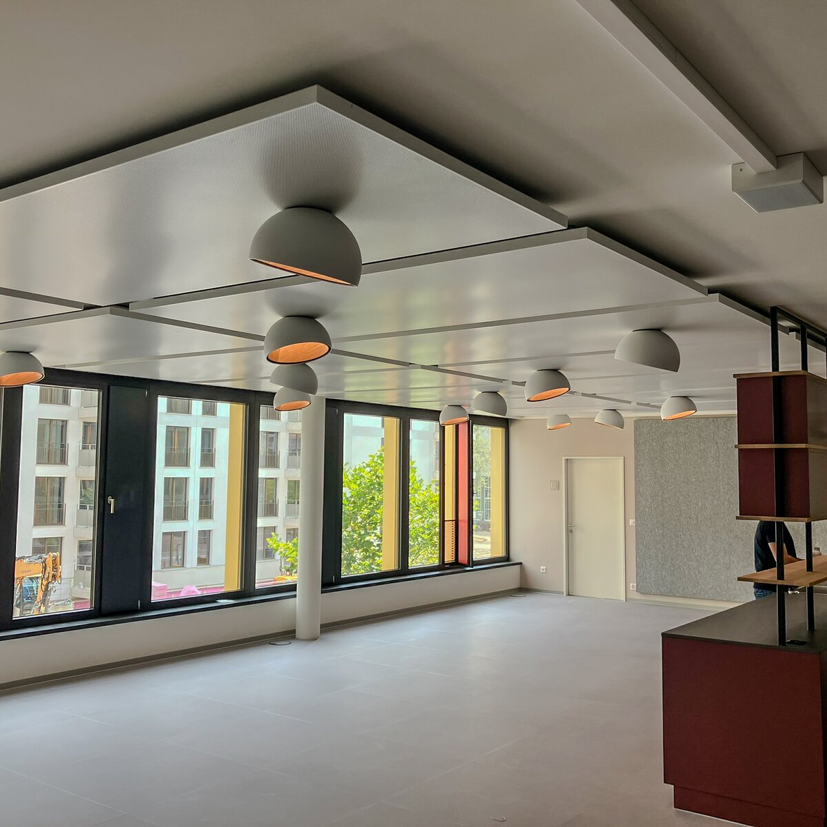 Leutschentower Oerlikon Innenraum: helle Büroräume mit linker Fensterfront, Lindner Plafotherm® Heiz-/Kühldeckensegel, moderne Leuchten, roter Regal-Raumteiler. | © © www.Lindner-Group.com