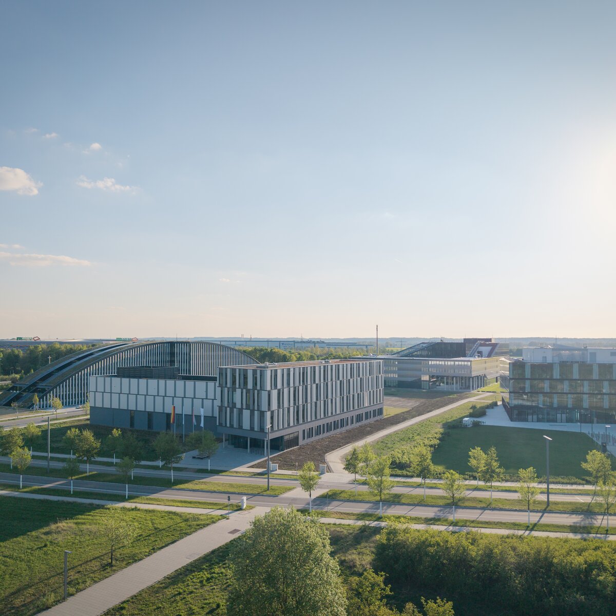 Drohnenaufnahme des DLR-Institutsgebäudes im Technologiepark Augsburg mit modernen Forschungs- und Büroflächen, umgeben von begrünten Außenanlagen unter sonnigem Himmel | © © www.Lindner-Group.com