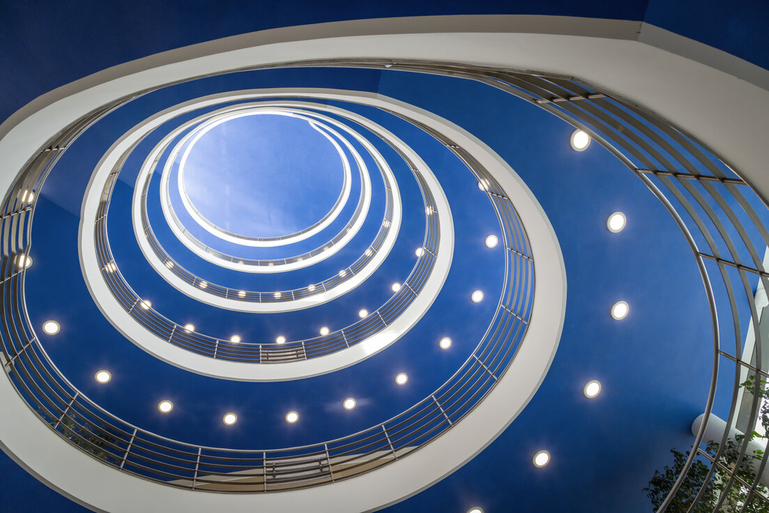 Runder, spiralförmiger Treppenaufgang im hbw München mit blauer Decke und deutlich sichtbaren, von Lindner auf LED umgerüsteten Downlights. | © © www.Lindner-Group.com