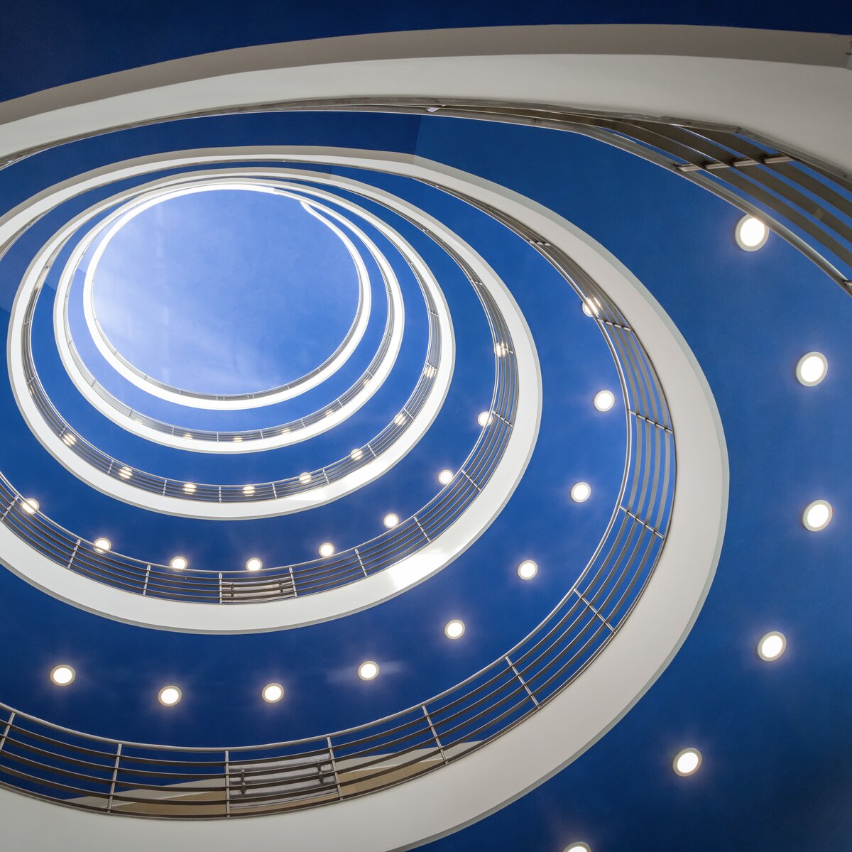 Runder, spiralförmiger Treppenaufgang im hbw München mit blauer Decke und deutlich sichtbaren, von Lindner auf LED umgerüsteten Downlights. | © © www.Lindner-Group.com