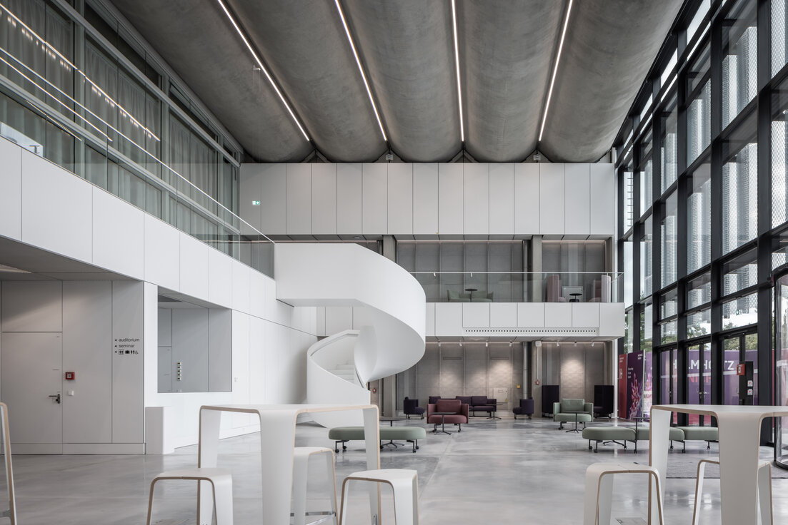 Modernisiertes Foyer des Helmholtz Zentrums München mit geschwungener Treppe, großflächiger Verglasung und modernen Sitzbereichen. | © © www.Lindner-Group.com