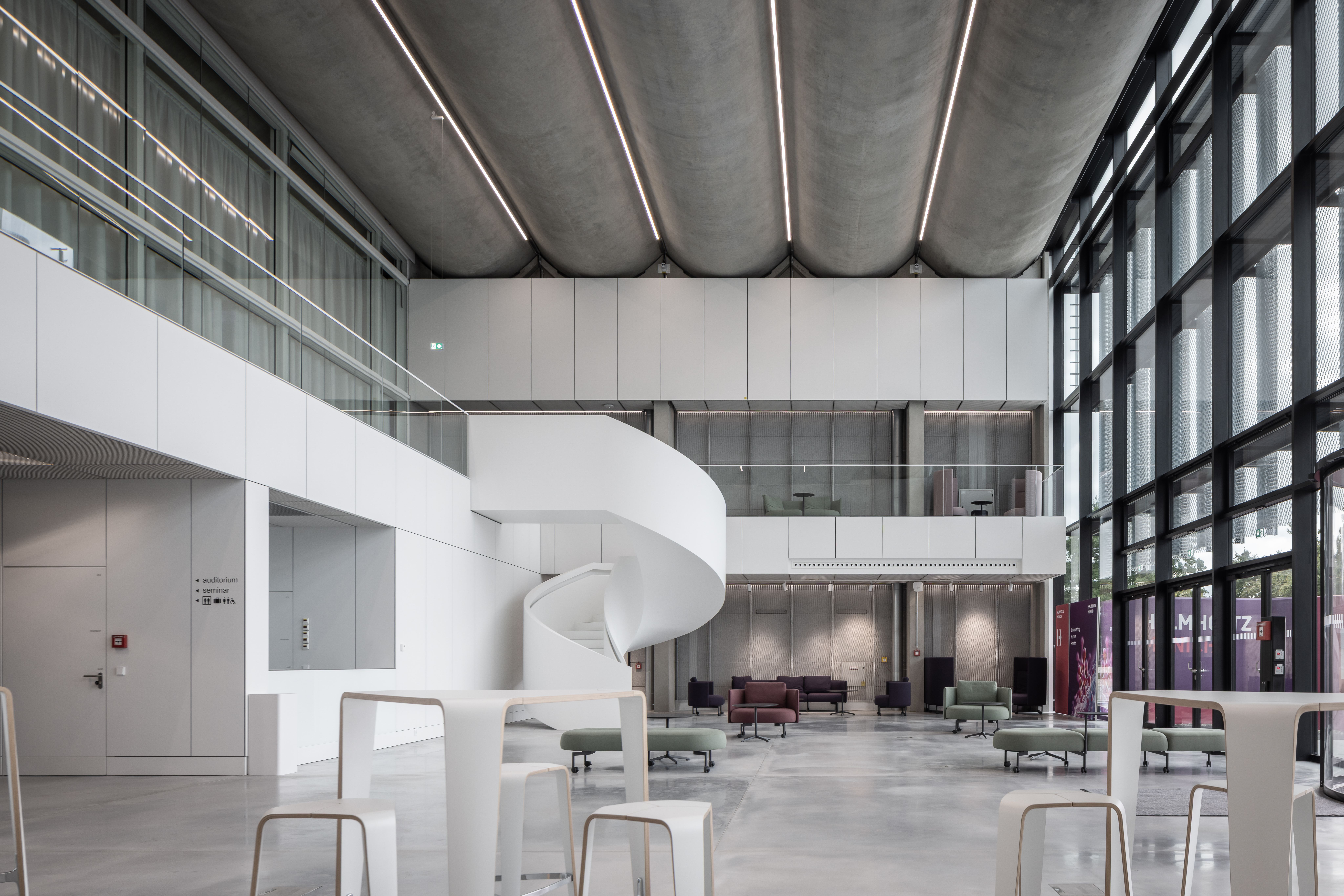 Modernisiertes Foyer des Helmholtz Zentrums München mit geschwungener Treppe, großflächiger Verglasung und modernen Sitzbereichen. | © © www.Lindner-Group.com