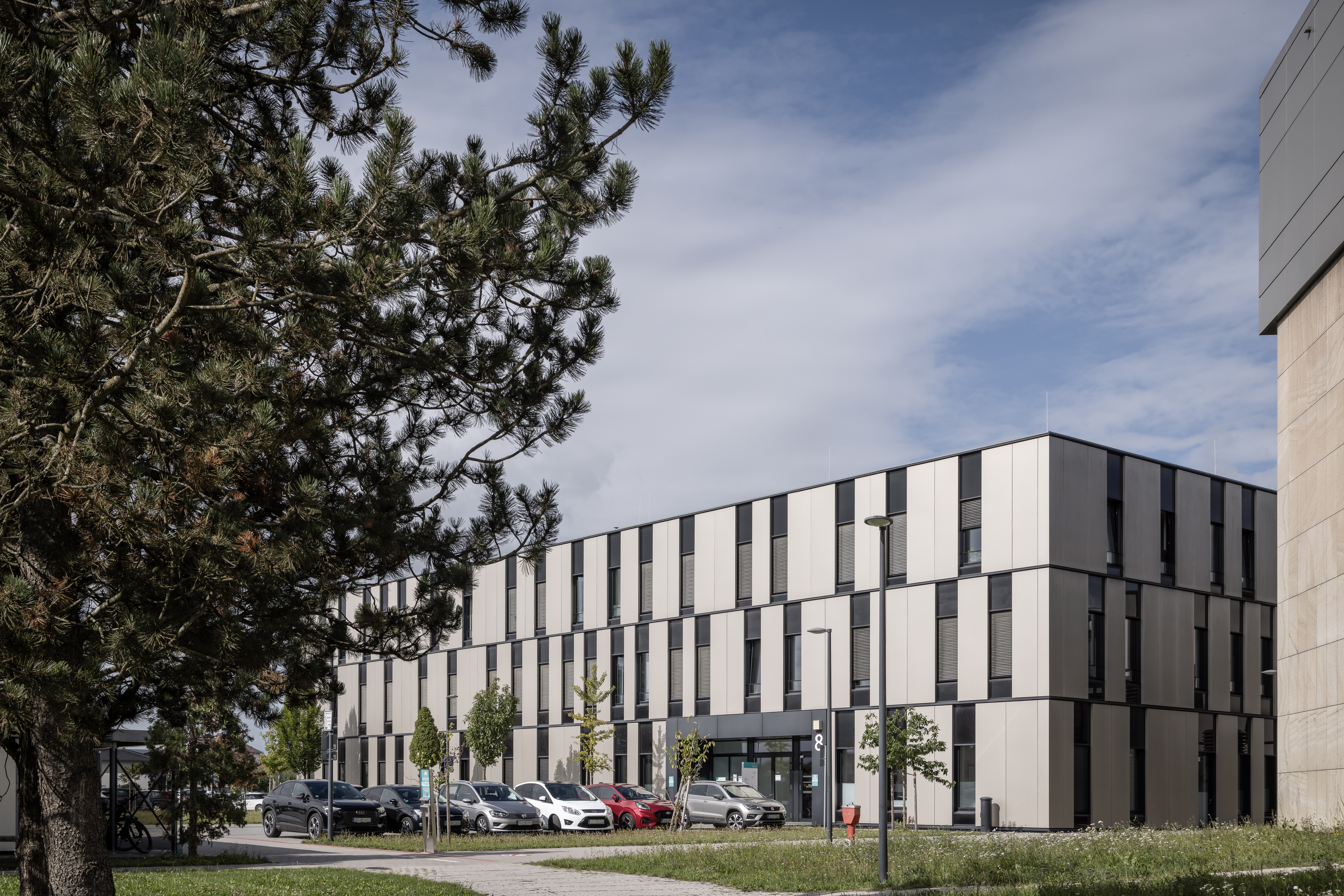 Außenansicht des InnKlinikums Altötting und Mühldorf in Altötting mit Parkplatz, Grünfläche und Bäumen; Lindner Group unterstützte den Umbau der Zentralapotheke mit eigenen Produkten. | © © www.Lindner-Group.com