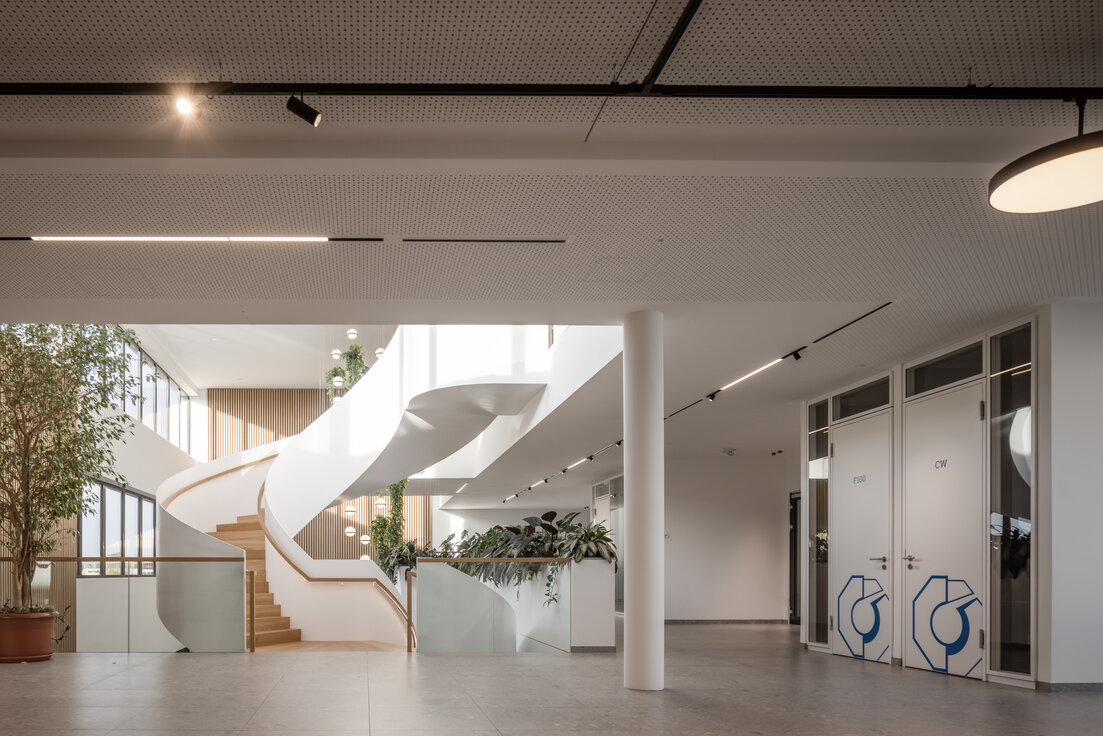 Elegante Wendeltreppe mit Glasfront im Neubau der Wack Group in Baar-Ebenhausen – helle, lichtdurchflutete Eingangshalle mit grüner Bepflanzung, Holzpaneelen und Lindner Holztüren HTB 41/49 mit Lichtauslässen | © © www.Lindner-Group.com