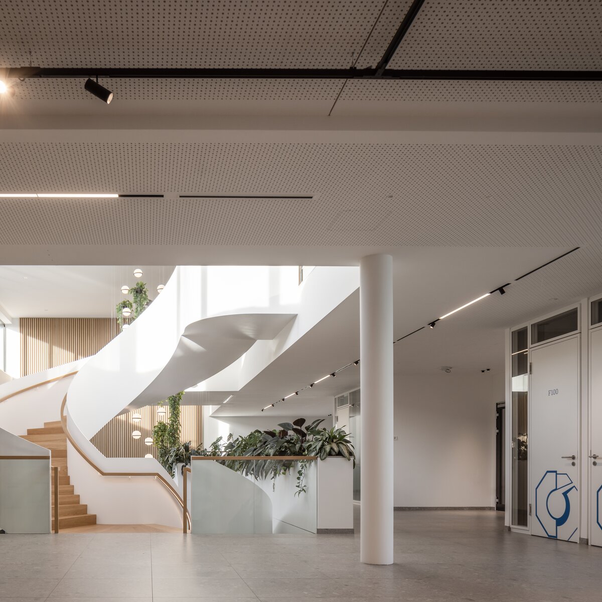 Elegante Wendeltreppe mit Glasfront im Neubau der Wack Group in Baar-Ebenhausen – helle, lichtdurchflutete Eingangshalle mit grüner Bepflanzung, Holzpaneelen und Lindner Holztüren HTB 41/49 mit Lichtauslässen | © © www.Lindner-Group.com