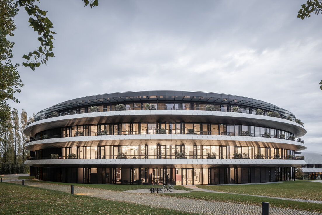 Außenansicht des ringförmigen Gebäudes „The Doughnut“ am Institut Le Rosey in der Schweiz mit Grünflächen und Gehwegen. | © © www.Lindner-Group.com
