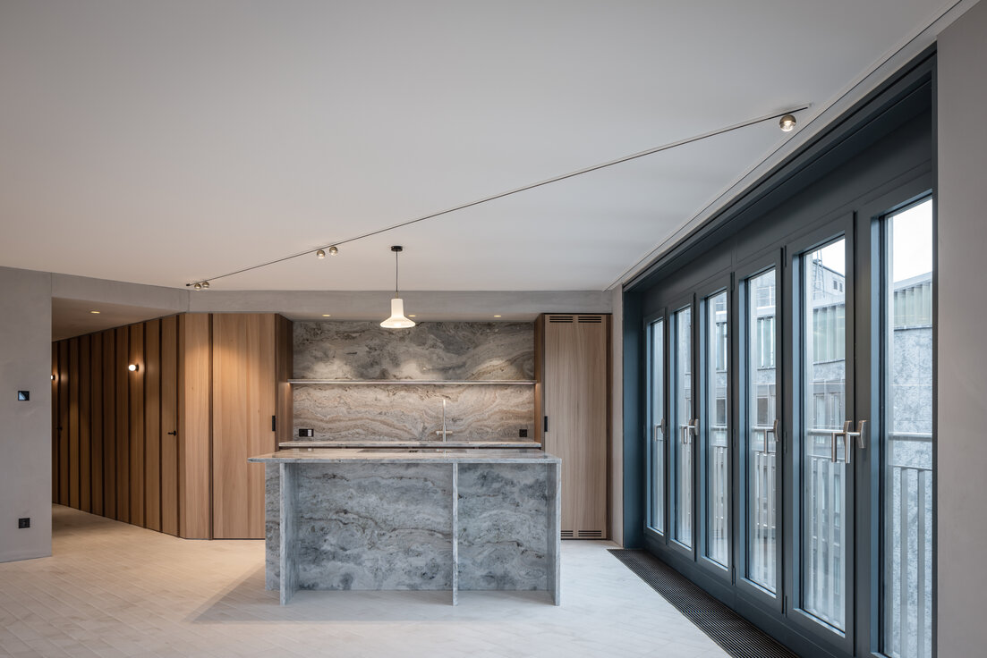 Moderner Küchenbereich mit heller Marmor-Kücheninsel, Fensterfront und hochwertiger Holzvertäfelung in stilvollem Innenraum | © © www.Lindner-Group.com