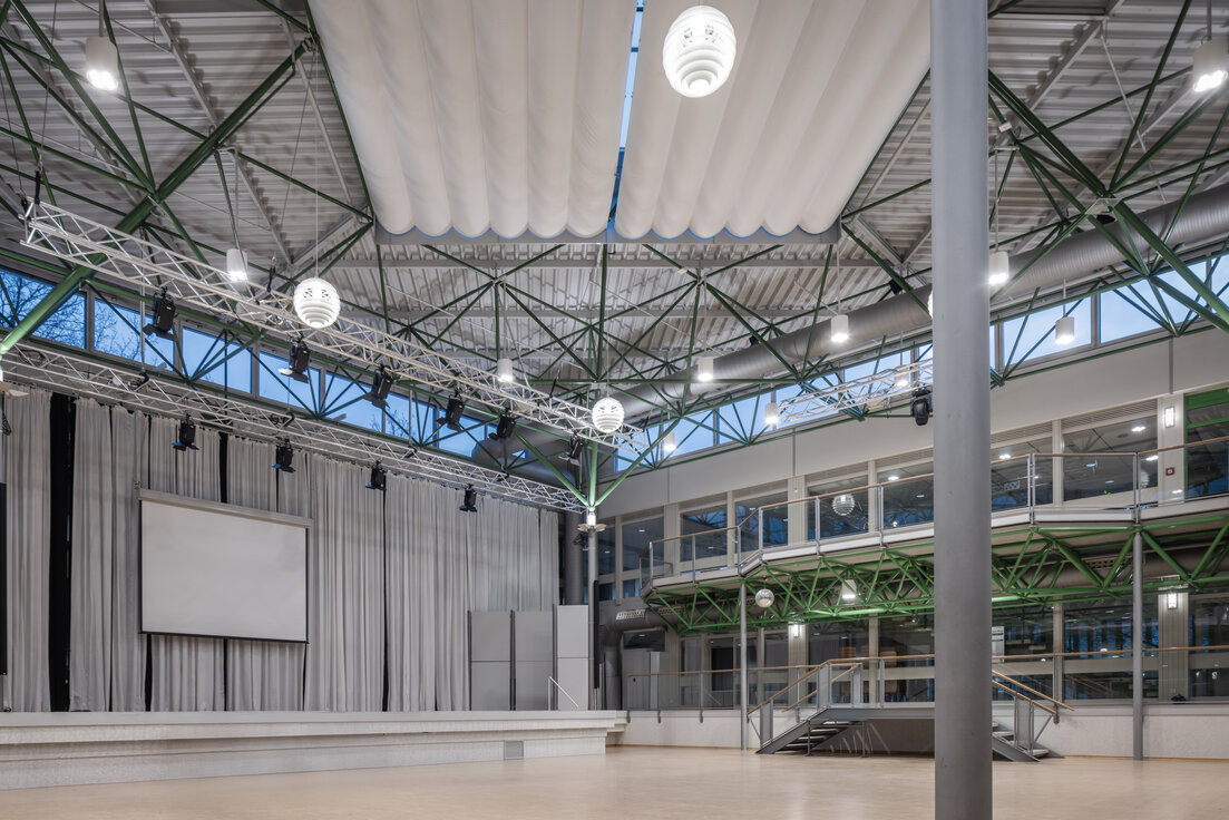 Atrium des Gymnasiums Vilshofen mit hängenden Leuchten, Bühne und Leinwand im multifunktionalen Veranstaltungsraum. | © © www.Lindner-Group.com