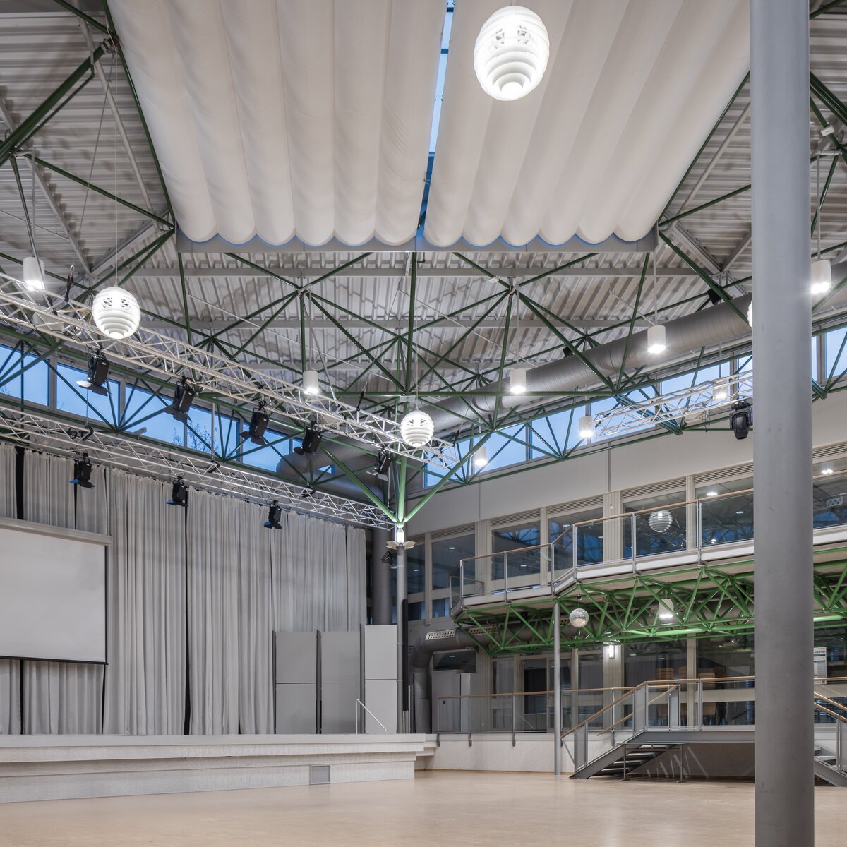 Atrium des Gymnasiums Vilshofen mit hängenden Leuchten, Bühne und Leinwand im multifunktionalen Veranstaltungsraum. | © © www.Lindner-Group.com